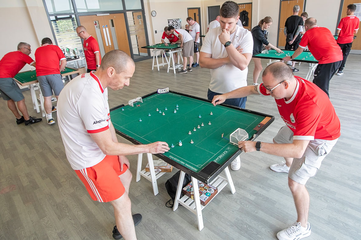 Subbuteo-by-Peter-Holmes A group of players around a subbuteo table during a match