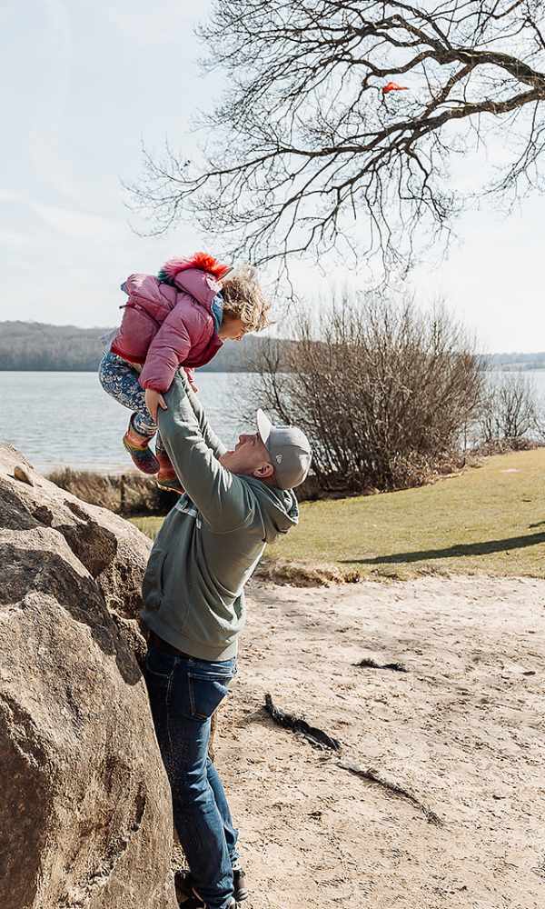 Bewl Man holding up child by a rock next to water